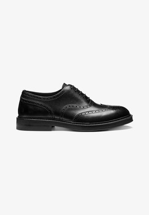 Zapato brogue de hombre de cuero negro con cierre cerrado, perforaciones decorativas y tacón apilado sobre fondo blanco.