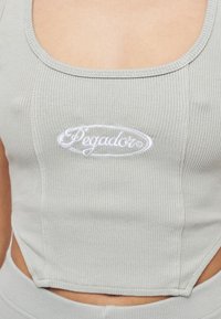 Grå ribbad crop top med fyrkantig halsringning, med en vit broderad "Pegador"-logotyp i mitten och sidöppningsdetalj.