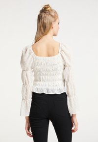 White puff-sleeve blouse featuring a smocked back and textured polka-dot fabric; worn with black fitted pants.