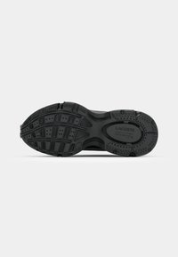 Black athletic shoe sole with textured rubber, deep treads, and grooves. Features Lacoste branding embossed on the side.