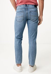 Jeans de mezclilla azul claro con un corte ajustado, que presentan dos bolsillos traseros y detalles de costura sutiles. Llevados con una camisa rosa y zapatillas blancas.