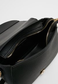 Czarna torebka ze skóry z fakturą, z złotym zamkiem błyskawicznym, o wyraźnie zarysowanym kształcie i gładkim wnętrzu, z kieszenią na zamek.