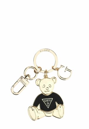 Llavero en tono dorado con un osito de peluche que lleva una camiseta negra con el logo de Guess, unido a un anillo y un cierre.