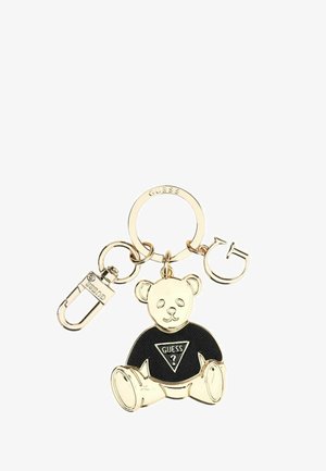 Llavero en tono dorado con un osito de peluche que lleva una camiseta negra con el logo de Guess, unido a un anillo y un cierre.