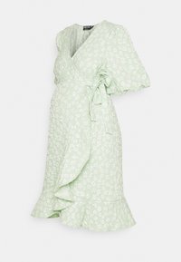 Vestido wrap verde claro com mangas curtas bufantes, apresentando um padrão floral, barra com babados e um laço lateral para ajuste.