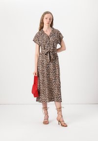 Rochie cu imprimeu de leopard, cu mangas scurte tip capă, curea în talie și fustă evazată. Accesorizată cu o geantă roșie și sandale cu barete nude.