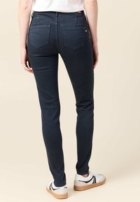 Jeans de mezclilla azul oscuro ajustados con una cintura de altura media, que presentan dos bolsillos traseros y detalles de costura sutiles, combinados con zapatillas blancas.