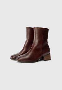 Brown leather ankle boots with a squared toe, smooth texture, and a stacked wooden heel. Sleek silhouette and minimal design details.
