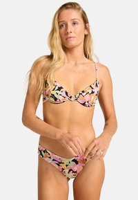 Conjunto de bikini con un patrón floral en rosa, amarillo y verde sobre un fondo negro; tirantes finos; tejido suave; parte inferior de cobertura mínima.