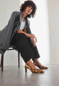 Leopardmönstrade slingback-klackar med spetsig t�å och blockklack, tillverkade av mjukt tyg. Bärs med svarta vida byxor och en grå blazer.