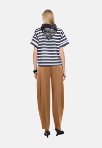 Top a righe bianche e nere con maniche corte, abbinato a pantaloni beige a vita alta e larghi. Gli accessori includono una sciarpa nera stampata.