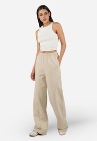 Beige brede joggebukser med sidesømmer og elastisk midje, sammen med en tettsittende hvit ribbet singlet med en subtil logo-detalj.