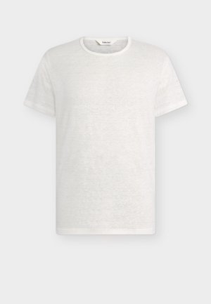 T-shirt blanc uni à manches courtes et col rond, en tissu légèrement texturé, sur un fond gris clair neutre.