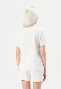 Hvit bomull t-skjorte sett fra ryggen, med kortermede ermer, klassisk rund hals og en avslappet passform. Glatt tekstur, minimal detaljer.