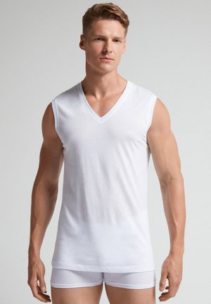 Hvid bomuldsærmeløs V-hals skjorte med en glat tekstur, fitted form og minimalistisk design, parret med hvide shorts.