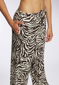 Pantaloni con stampa zebra marrone e crema, dotati di vita elasticizzata, coulisse e tasche laterali. Tessuto leggero con una vestibilità rilassata.