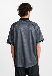 Szara koszulka polo z krótkim rękawem w geometryczny wzór. Posiada czarny kołnierzyk i paski na rękawach. Gładka tekstura.