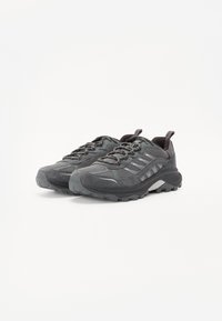 Gray athletic shoes with mesh and suede materials, featuring prominent rubber soles, textured accents, and lacing system.