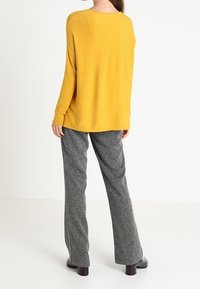 Un pull surdimensionné jaune associé à un pantalon large texturé gris, avec une encolure ronde et des manches longues, vu de dos.