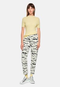 Yellow ribbed short-sleeve sweater, white jeans with black tiger stripes, and silver sneakers with light yellow socks.