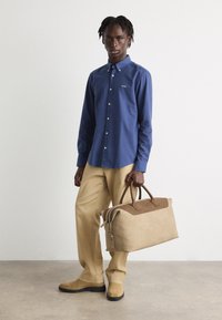 Marine knoop shirt, beige broek en bruine suède boots. Tan duffel tas met bruine accenten, gladde textuur en stevige handvatten.