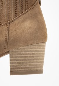 Brązowe zamszowe botki na kostkę z prążkowanym obcasem typu blok, prezentujące elegancki design i teksturowaną cholewkę z przeszyciami.