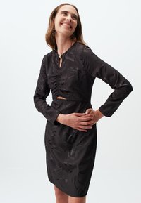 Zwarte jurk met lange mouwen en een cropped ontwerp, met een gerimpelde voorkant, bloemenstructuur en een keyhole halsopening.
