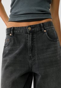 Jeans in denim neri a vita alta con una vestibilità leggermente ampia, dotati di bottoni in rame e due tasche anteriori. Leggero effetto sbiadito visibile.