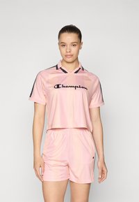 Roosa lühikeste varrukatega jersiga, millel on horisontaalsed triibud, mustad detailid ja logo; koos roosade lühikeste pükstega, mis on valmistatud kergetest materjalidest.