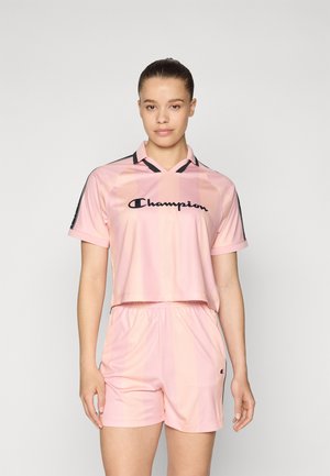 Pink cropped jersey with horizontal stripes, black accents, and logo; paired with matching pink shorts, both made of lightweight material.