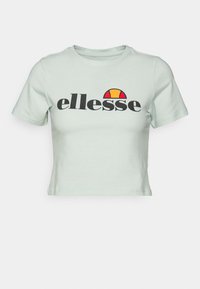 Camiseta recortada de color verde menta hecha de algodón, con mangas cortas y un logotipo negro en contraste con un diseño rojo y amarillo encima.