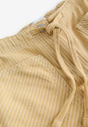 Gule shorts med striber og snøre i taljen. Har en lomme med lap og tekstureret stof. Syninger er synlige langs kanterne.