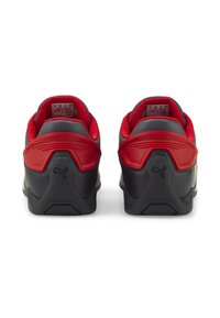 Czarne i czerwone buty sportowe z teksturowanymi powierzchniami, wyściełanymi kołnierzami i logotypem na pięcie. Projekt charakteryzuje się kontrastującymi materiałami i akcentami.
