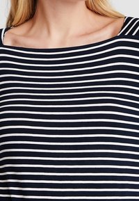 Gestreiftes Oberteil in Marineblau und Weiß mit weitem Ausschnitt, aus einem weichen, leichten Stoff mit glatter Textur und gleichmäßig verteilten horizontalen Linien.