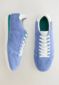 Modré semišové tenisky s bílými tkaničkami, zelenými akcenty a bílou gumovou podrážkou. Mají elegantní design a strukturovaný povrch.