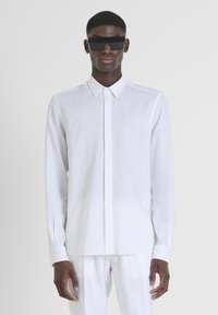 Camicia bianca a maniche lunghe realizzata in tessuto leggero, con chiusura a bottoni, colletto puntato e polsini. Gli occhiali da sole neri completano il look.