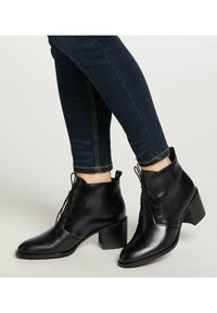 Bocanci de piele negri, până la gleznă, cu vârf rotund, design cu șireturi și toc mediu pătrat, asortați cu blugi skinny de denim închis la culoare.