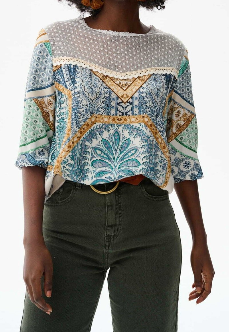 Blouse imprimée à manches courtes ; présente des motifs bleus, verts et dorés ; encolure en voile à pois ; designs floraux complexes ; coupe décontractée.