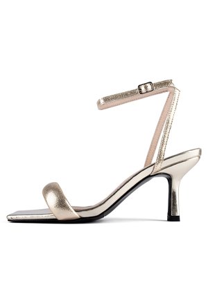 Sandale à talon haut métallique dorée avec un bout carré, une sangle de cheville avec une boucle et une sangle texturée. Fini lisse et design de talon fin.