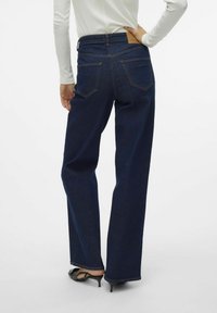 Bredbeniga blå denimjeans med hög midja, synliga fram- och bakfickor samt en brun läderlapp på bakre midjebandet.