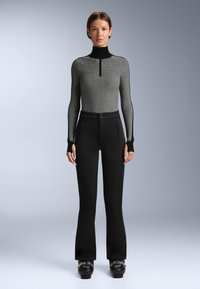 Crna i siva rebrasta pletena majica s visokim ovratnikom, uparena s crnim hlačama s flare krojem koje imaju dva prednja džepa i suptilne detalje šivanja.
