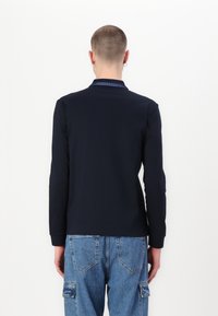 Ναυτικό μπλουζάκι πόλο με μακριά μανίκια και αντίθετο γιακά, εφαρμοστή σχεδίαση, λεία υφή και μινιμαλιστικό στυλ, σε συνδυασμό με ανοιχτόχρωμο τζιν cargo παντελόνι.