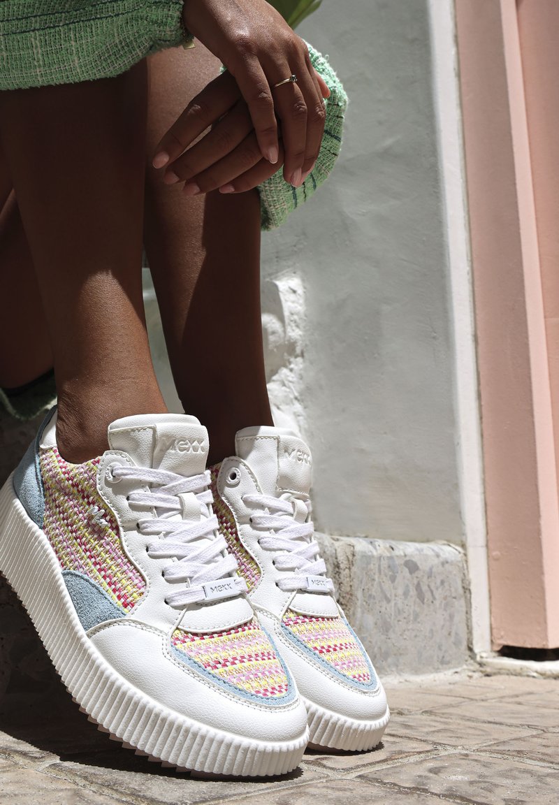Witte sneaker met multiculturele geweven stofaccenten, gestructureerde zolen en lichtblauwe details. Rond neuzen en vetersluiting.