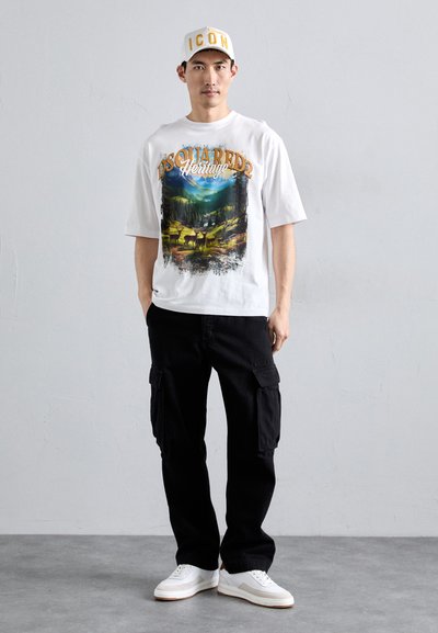 Hvid kortærmet T-shirt med et farverigt grafisk print af et landskab. Sorte cargo bukser og hvide sneakers med en beige sål. Kasket med teksten "ICON".