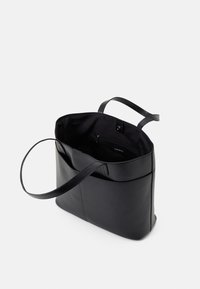 Svart läderhandväska med en strukturerad form, två handtag och en rymlig insida som har ett dragkedjefack. Slät textur.