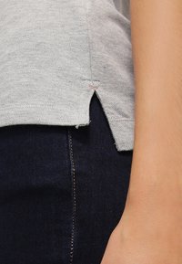 Ljusgrå T-shirt med sidoflik, i bomullstyg, med en subtil textur och kontrasterande orange sömmar nära nederkanten.