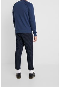 Marineblauwe sweatshirt met geribbelde manchetten en zoom, voorzien van een gestructureerd schouderdetail, gecombineerd met marineblauwe streepbroek en zwarte schoenen.