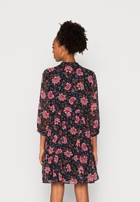 Vestido floral em tecido preto com padrões de flores em rosa e azul. Apresenta uma bainha com volantes e mangas três quartos, com uma gola alta.