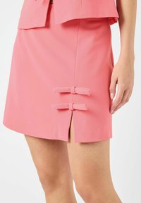 Rosa miniskjørt med doble sløyfeakcenter, en sideglipp og en jevn tekstur. Skreddersydd passform med rene linjer.