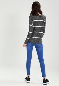 Gestreifter Pullover in Schwarz und Weiß, gestrickte Textur, lockere Passform. Kombiniert mit blauen Skinny-Jeans. Sneakers mit schwarzen und aquafarbigen Akzenten.